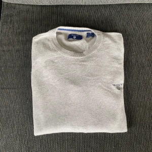 Grå stickad tröja från GANT - Säljer en stilren grå stickad tröja från GANT i barn storlek M. Tröjan har rund halsringning, diskret broderad logga på bröstet och är långärmad. Perfekt för dig som gillar klassisk och enkel stil. Materialet är mjukt och skönt mot huden.