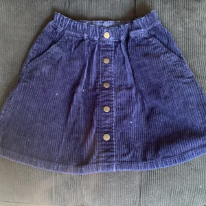 Mörkblå manchesterkjol från Uniqlo - Supersnygg mörkblå kortkjol i manchester från Uniqlo. Kjolen har knappar framtill och två fickor🤍Storleken säger 7-8 år, men eftersom midjan är stretchig passar den även mig som brukar ha storlek XS-S i kjolar💞 Kjolen är i bra skick förutom lite slitningar på knapparna som inte är märkbart om man inte tittar nära💞