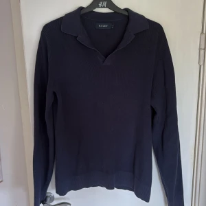 Mörkblå stickad tröja från Riley - Säljer en mörkblå stickad tröja från Riley i storlek S. Tröjan har en klassisk krage med v-ringning och långa ärmar. Den är ribbstickad och har en stilren, enkel design som passar perfekt till jeans eller chinos.