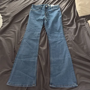 Blå bootcut jeans från H&M - Säljer ett par blå jeans från H&M med flared/bootcut-ben och låg midja. Jeansen har justerbar midja och klassisk femficksdesign.  Materialet är klassisk denim. Pris kan diskuteras vid snabb affär.