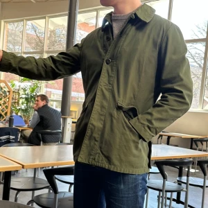 Swedish Vintage Army Field Jacket 70s - Sällsynt vintage militärjacka/overshirt från 70-talet i klassisk grön färg. Stora fickor med lock fram och bak, knäppning med knappar. Bärs som jacka eller overshirt. Fint skick utan hål. Perfekt för dig som gillar army, workwear eller vintage med karaktär.  Mått: Bröstvidd: 57 cm Armlängd: 65 cm Rygglängd: 75 cm 