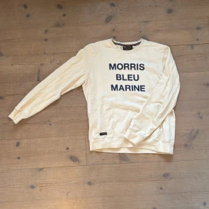 Vit sweatshirt från Morris med tryck - Säljer en vit sweatshirt från Morris med mörkblå text 'MORRIS BLEU MARINE' på bröstet. Tröjan har rund halsringning, långa ärmar och ribbade muddar. Skön och stilren, perfekt till jeans eller shorts. 