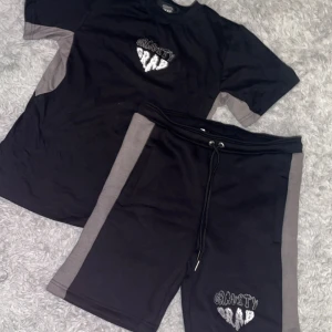 Svarta shorts Gravity Rap med gråa detaljer - TikTok kända!! Svarta shorts och t shirt  från Gravity Rap med gråa paneler på sidorna och broderad logga framtill. De har snörning i midjan för perfekt passform och är gjorda i mjukt bomullsmaterial. Dem är ej använda alls! Prislappen är kvar! Säljer 1 för 600 men settet kan jag släppa för 1000kr! För mer bilder skriv dm! 