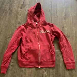 Röd hoodie från Branäsgruppen XS - Snygg röd hoodie från Branäsgruppen med dragkedja och huva. Tröjan har fickor framtill och vit text med Branäs-logga på bröstet. Perfekt för dig som gillar en sportig och avslappnad stil.