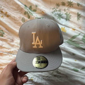 Grå LA New Era 59FIFTY keps 7 3/8 - Snygg grå New Era 59FIFTY keps med LA-logga broderad framtill i vitt. Klassisk flat peak och broderad MLB-logga bak. Tillverkad i bomull och polyester, perfekt för dig som gillar streetwear och sportig stil. Knappt använda är vilig att gå ner i pris därför väljer jag att starta på 350