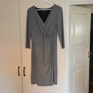 Mönstrad draperad klänning från Ralph Lauren - Snygg ,knappt använd klänning från Ralph Lauren med geometriskt mönster i mörkblått och vitt säljes. Klänningen har  v-ringning, lång ärm och markerad midja med drapering. Mjuk och stretchig känsla, perfekt för dig som gillar klassisk men cool stil. Klänningen är i mycket gott skick !