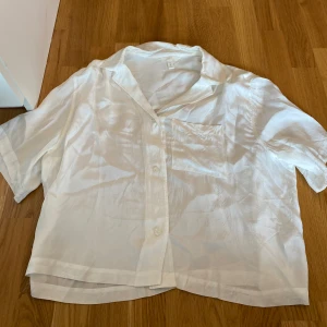 Vit kortärmad skjorta i silke i strl M - Snygg vit skjorta från H&M i silkesliknande material. Skjortan har korta ärmar, klassisk krage, bröstficka och knäppning framtill.  I strl M från H&M