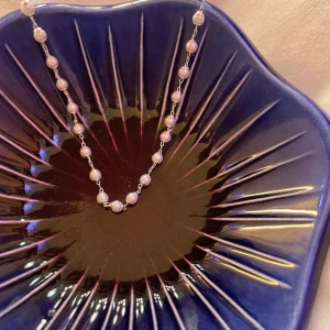 Pärlhalsband med silverkedja - Stilrent halsband med små vita pärlor jämnt fördelade längs en tunn silverfärgad kedja. Perfekt för dig som gillar klassiska smycken med en modern twist. Kedjan är tunn och smidig, och pärlorna ger ett elegant intryck.