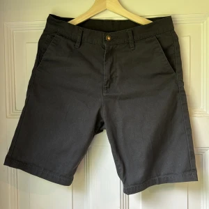 Mörkgrå shorts från Sweet SKTBS - Klassiska mörkgrå shorts från Sweet SKTBS med normal passform. De har fickor fram och bak, bälteshällor och stängs med knapp och dragkedja. Materialet är en mix av polyester och bomull, vilket gör dem både bekväma och slitstarka. Perfekta för sommardagar.