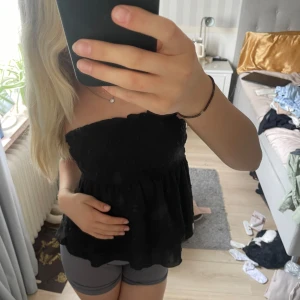 Svart bandeau tubtopp med volang - Supersöt svart bandeau tubtopp med smockad överdel och volangig nederdel. Toppen är ärmlös och har små diskreta prickar i tyget som ger en extra touch. Perfekt för dig som vill ha en luftig och trendig look i sommar. Kommer från shein och är i storlek XS. 