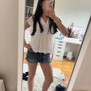 Blå jeansshorts med fransig kant - Säljer ett par klassiska blå jeansshorts med fransig kant nertill. De har normal passform, fem fickor och bälteshällor. Perfekta för sommaren och lätta att matcha med allt. Snygg slitning och tidlös look.