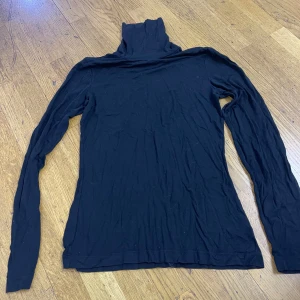 Svart polotröja från Lindex - En svart, klassisk polotröja från Lindex i storlek S. Tröjan är långärmad och har en tight passform med hög polokrage. Tillverkad i mjuk bomull, perfekt att styla med jeans eller kjol för en clean look.