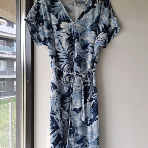 Blommig klänning linne viskos H&M S/M blue floral oldschool vintage resort 90s 00s y2k - Snygg blåvit midi sommarklänning med tropiskt blommönster, v-ringning och korta ärmar. Knytband i midjan för en skön passform. Använd en gång. Tillverkad i en luftig mix av viskos och linne, perfekt för varma dagar. S enligt lappen men stor i storleken, passar som M. 20% linne, 80% viskos
