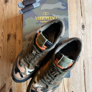 Valentino Garavani Rockrunner sneakers - Snygga Valentino Garavani Rockrunner sneakers med camouflage-mönster i grönt, beige, svart och orange. Skorna är köpta från Plick och varit sparasamt använda från mitt håll. Skorna är slitna men för det mesta på insida häll. Skolådan och extra skosnören ingår. Har ni några frågor är det bara att skriva. 
