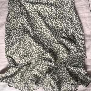Blommig volangkjol från Vero Moda - Superfin kjol från Vero Moda i storlek S med vitblommigt mönster på grön botten. Kjolen har volangdetaljer nertill som ger en flowy känsla och är perfekt för vår och sommar. ☀️Lätt och luftig, passar till sneakers eller sandaler.
