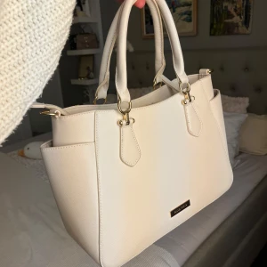 beige väska med gulddetaljer från Anna Field - Jag säljer min älskade beiga väska med gulddetaljer från Anna field!✨ Väskan är stor och får plats med mycket och är i bra skick men det är lite sminkfläckar inuti väskan💗Har även ett längre band man kan sätta på eller av enkelt beroende på om man vill ha den lång eller inte :)