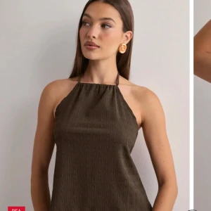 Brun topp med öppen rygg - Snygg brun topp med halterneck och öppen rygg. Klänningen har knytband i nacken och baktill, samt en lätt strukturerad yta. Perfekt för varma dagar och ger en trendig look.