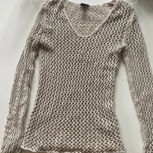 Beige stickad långärmad tröja  - Säljer en beige stickad tröja från H&M i storlek S. Tröjan har ett grovmaskigt nätmönster, v-ringning och långa ärmar. Den är ganska lång och perfekt att styla över ett linne eller bikini för en chill och trendig look.