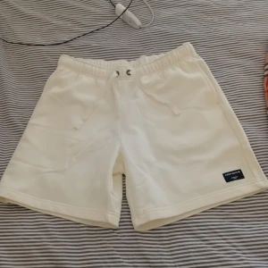 Vita shorts från Björn borg  - Snygga vita shorts från Björn Borg med elastisk midja och snörning. De har en enkel och clean look med en liten svart logotyp-patch på benet. Perfekta för sommardagar eller chill hemma. Materialet känns mjukt och bekvämt.