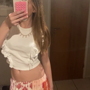 Vit croppad topp med volangdetaljer - Säljer en vit croppad topp med volangdetaljer på sidorna. Toppen har korta ärmar och är perfekt för varma dagar. Enkel och stilren design som passar till mycket. Tror den är i storlek 152 men passar som xs