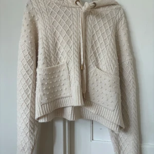 Beige stickad hoodie från Zara - Superfin beige stickad hoodie från Zara med snyggt kabelstickat mönster och två fickor framtill. Tröjan är croppad och har dragsko i huvan. Perfekt för mysiga dagar och enkel att styla till jeans eller kjol. Pris går att diskutera