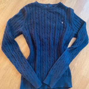 Svart kabelstickad tröja från GANT - Säljer en mörkblå kabelstickad tröja från GANT i stretchig bomull. Inga defekter och inte använd mycket