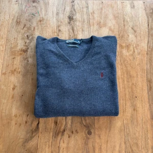 Polo Ralph Lauren – Mörkgrå ulltröja i lamull - Värmande och stilren V-ringad tröja i 100% lammull med vinröd broderad logga.  Storlek: M (normal i storlek) Färg: Mörkgrå med vinröd logga Material: 100% lamull Skick: Mycket fint skick – inga hål eller fläckar Stil: Klassisk / Preppy / Vintage Passform: Rak modell med V-ringning och ribbade muddar Nypris: ca 1 500 kr Pris: 350 kr  Frakt: Skickas snabbt & spårbart