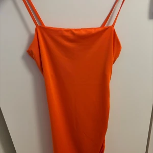 Orange axelbandsklänning med rynkade detaljer - Säljer en snygg orange klänning med smala axelband och rynkade detaljer längs sidan. Klänningen har ett  mjukt, stretchigt material som känns skönt mot huden. 