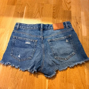 Blå jeansshorts  - Säljer ett par blå jeansshorts. Snygga slitningar både fram och bak, avslappnade i låren. 