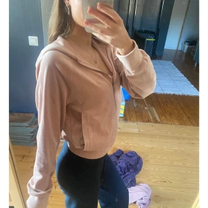 Ljusrosa hoodie med dragkedja - Säljer en ljusrosa hoodie med dragkedja och huva. Velourjacka har långa ärmar, ribbade muddar och är i ett mjukt material. Perfekt för en avslappnad stil.