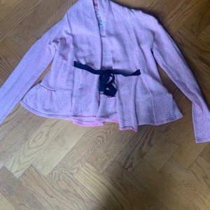 Rosa omlottjacka från Odd Molly - Säljer en ljusrosa omlottjacka från Odd Molly med knytband i midjan. Koftan har ett diskret mönster och långa ärmar. Perfekt för lager-på-lager och ger en feminin touch till din outfit. Storleken står inte men den passar en person som har Xs-S.