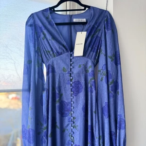 Lila/blå blommig klänning från Adoore - Superfin långklänning i lila/blå från Adoore med blommigt mönster. Helt ny. Storlek 32.