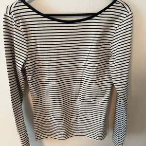 Randig långärmad topp från Lindex - Säljer en klassisk långärmad topp från Lindex i vitt med svarta tunna ränder. Toppen har rundad halsringning med svart kant och är i ett mjukt, stretchigt material. Perfekt basplagg till garderoben! Den har en uringad rygg 