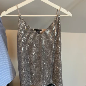 Glittrig fest blus🌟 - Supersnygg glittrig silvertop från Amisu med tunna justerbara axelband. Perfekt för dig som vill sticka ut med en festlig look. Toppen har en rak passform och är täckt av paljetter som fångar ljuset. Endast använd en kväll💞