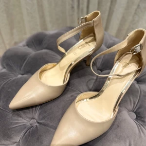 Beige pumps med ankelrem och spetsig tå, Bata - Används bara 1 gång. Säljer ett par eleganta beige pumps med smal klack och spetsig tå. Skorna har en justerbar ankelrem med spänne och är tillverkade i ett slätt material som ger en stilren look. Perfekta för dig som vill ha en klassisk och trendig sko.