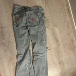 Ljusblå bootcut jeans med slitningar - Säljer ett par ljusblå bootcut jeans med slitningar på båda knäna och rosa detaljer på bakfickorna. 