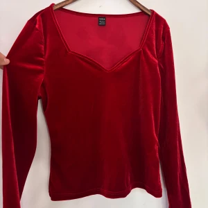 Röd sammets topp med v-ringning från Shein - Säljer en röd långärmad topp i mjuk sammet från Shein. Toppen har en snygg v-ringning och figurnära passform, perfekt för att lyfta din outfit med lite extra färg.