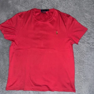 Röd t-shirt från Ralph Lauren - Snygg röd t-shirt från Ralph Lauren med klassisk broderad logga på bröstet. T-shirten har rund halsringning och korta ärmar. Perfekt för en stilren och avslappnad look.