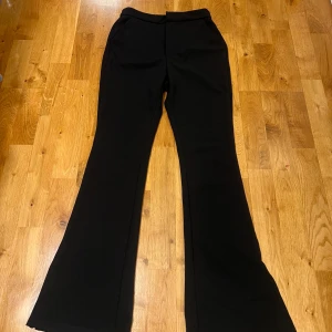 Svarta bootcut kostymbyxor med slits - Svarta utsvängda kostymbyxor och slits nertill på benen. Byxorna har hög midja, fickor på sidor och diskreta fickor bak. Oanvända men saknar lapp. Passar Xs-s.