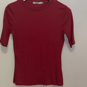 Mörk rosa ribbad topp från NA-KD - Säljer en röd ribbad topp från NA-KD med rund halsringning och korta ärmar. Toppen har en tight passform och är perfekt att styla till olika outfits. Enkel och stilren design.