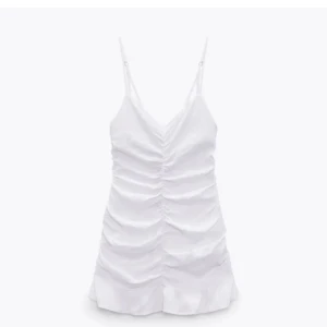 Vit linneklänning med volang från Zara - Superfin vit kortklänning i linne från Zara med smala axelband och snygg rynkdetalj framtill. Klänningen har volang nertill och en figurnära passform som ger en fräsch och somrig look.