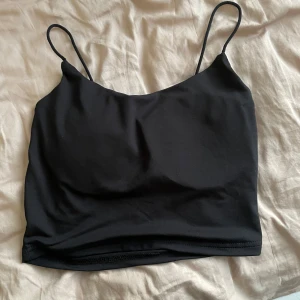 Svart croppad linnetopp med tunna axelband - Säljer en svart croppad linnetopp med tunna axelband och snygg öppen detalj i ryggen med knyt. Perfekt för sommaren och enkel att matcha till olika outfits. Kuppar inlagda. 