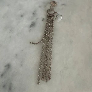 Silverfärgad kedjeaccessoar med kristalldetalj - Säljer en snygg accessoar i silverfärg med flera kedjor och en glittrande kristall-liknande detalj. Perfekt att fästa på väskan eller som nyckelring för en extra touch av stil.