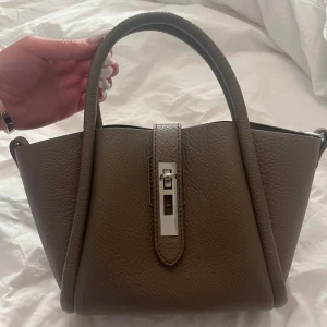 Väska Gina tricot - Skitsnygg beige/brun handväska från Gina Tricot!! Jättebra skick som ny, knappt använd. Den rymmer mycket skulle jag säga. Säljer pga att jag har för många väskor och denna inte kommer så mycket till användning💕köpt för 400kr.