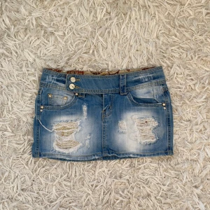 Blå jeanskjol med slitningar - Absolut snyggaste korta lågmidjade jeanskjolen! Perfekt nu till sommaren och så cool och unik. Säljer då den tyvärr är för liten. Midjemått: 38cm, längd: 26-29cm. Storlek 28 USA, 42 IT, jag tycker den passar xs- men se mått!