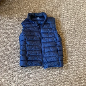 Svart dunväst från Uniqlo - Säljer en Svart dunväst från Uniqlo Ultra Light Down. Västen är lätt, har hög krage och horisontella sömmar. Perfekt för lager-på-lager, nu till våren och enkel att bära med sig tack vare sin lätta design.