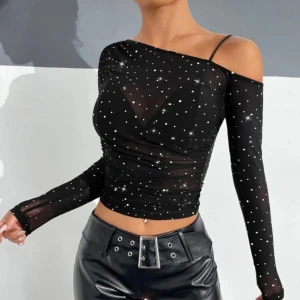 Svart mesh topp med strass och oneshoulder - Trendig svart mesh topp med glittrande strassdetaljer. Toppen har lång ärm, croppad passform och en axelbandslös design på ena sidan samt smalt axelband på andra. Perfekt för att sticka ut i mängden.