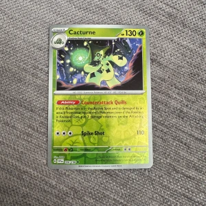Pokémonkort Cacturne - Säljer ett Pokémonkort med Cacturne från Sword & Shield-serien. Kortet har grön bakgrund och visar Cacturne i en mörk skogsmiljö. HP 130, attacken Spike Shot och förmågan Counterattack Quills. Perfekt för samlare eller Pokémonfans!
