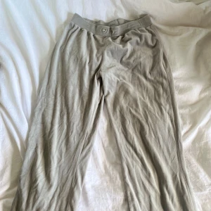 Beiga mjukisbyxor från Gina Tricot - Säljer ett par beiga mjukisbyxor från Gina Tricot i mjukt material. Byxorna har bred resår i midjan med två dekorativa öljetter framtill. Perfekta för en avslappnad stil. Snörena har jag tagit bort och hittar tyvärr inte de