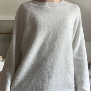 Vit stickad tröja med rund hals - Mysig vit stickad tröja med rund halsringning och långa ärmar. Tröjan har en enkel och stilren design, perfekt för lager-på-lager och passar till många olika outfits.